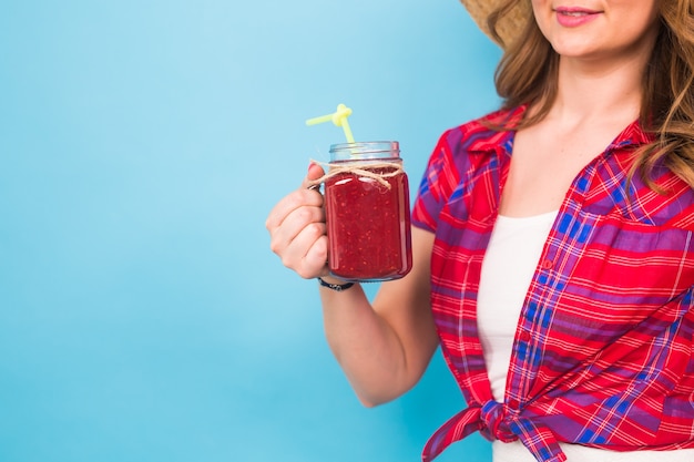 Primo piano di una donna che tiene in mano un succo di frutta o un cocktail su sfondo blu e copia spazio