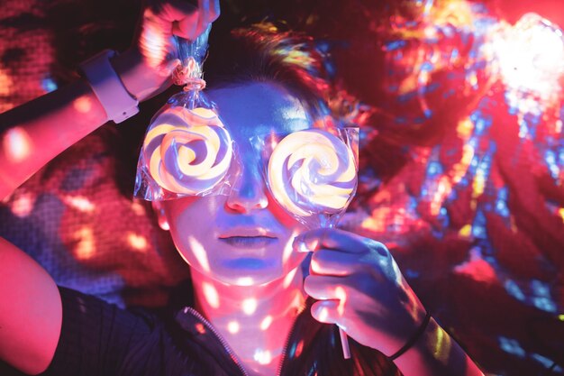 Close-up of woman holding lollipops while lying on bed in illuminated room