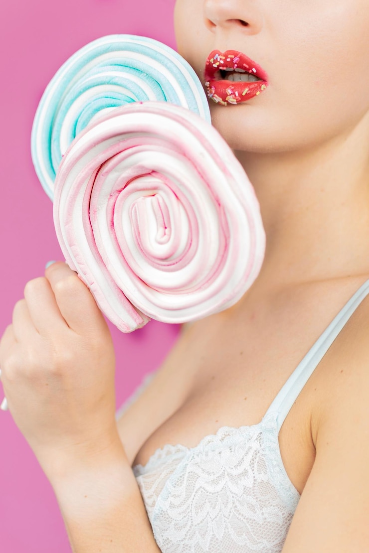 Photo close-up of woman holding lollipops while standing against pink background