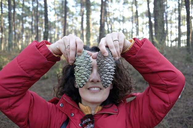 Foto donna in primo piano che tiene una cono di pino contro gli alberi