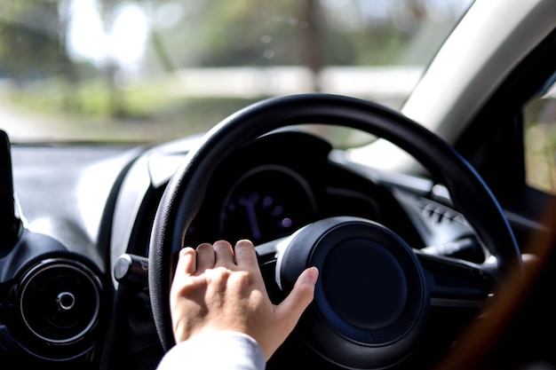 Close-up woman holding the steering wheel of a car, she is driving a car for a trip to the countryside, she is holding the steering wheel to steer the car and intends to drive safely.