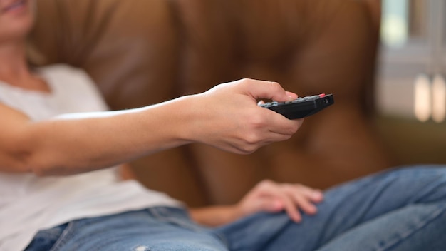 Close up of woman holding tv remote switching channels and relaxing on couch at home female