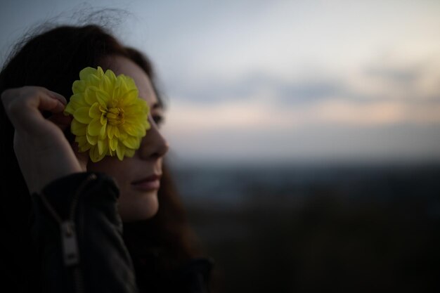 Foto close-up di una donna che tiene un fiore giallo contro il cielo durante il tramonto