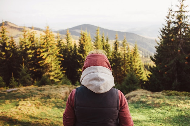 A close-up woman is standing in a jacket with a pink hood and a sleeveless jacket and is looking at the mountains.