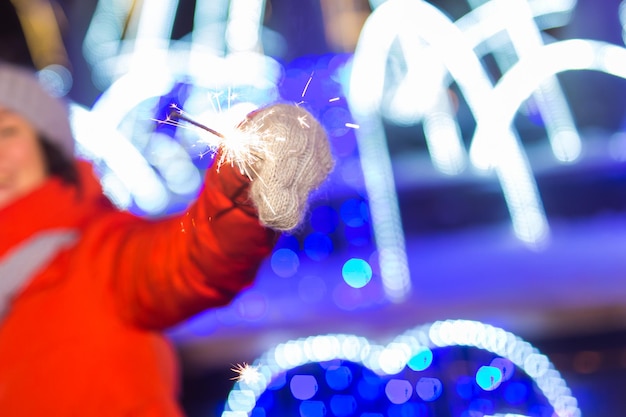 ベンガルの光、線香花火で街に立っているニット帽とスカーフのクローズアップ女性。コンセプトのお祝いとクリスマス。