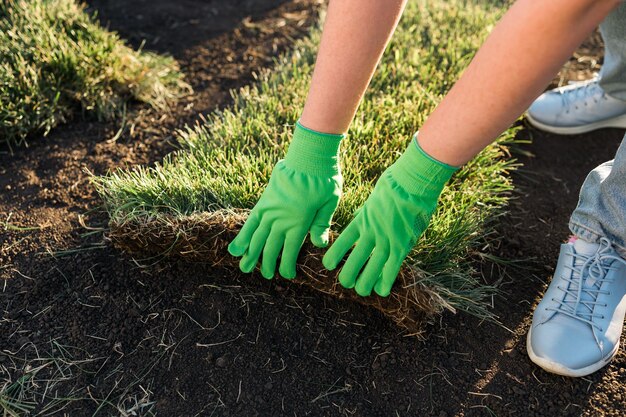 新しい庭の芝生の芝生の敷設の概念のために切り芝を敷設する女性をクローズアップ