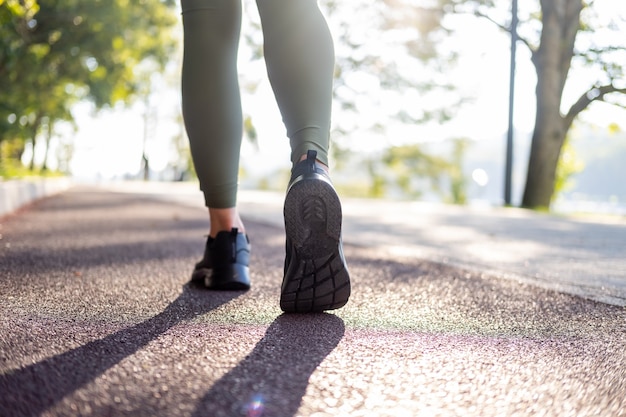 日の出の時間に公園で実行されているスポーツスニーカーで女性の足をクローズアップ健康的なフィットネスライフスタイル