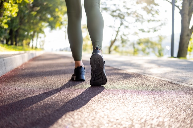 日の出の時間に公園で実行されているスポーツスニーカーで女性の足を閉じます。健康的なフィットネスライフスタイル。