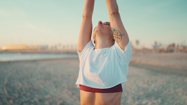 Foto primo piano donna che guarda fare yoga all'aperto ragazza tatuata sana che si allunga durante la lezione di yoga sul mare