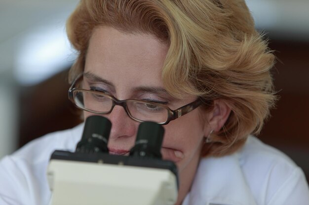 Клоуз-ап женщины, смотрящей через микроскоп в лаборатории