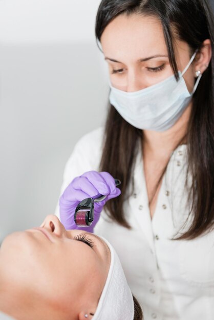 Foto close-up di una donna sdraiata con un estetista che usa un rullo cosmetico sul viso alla spa