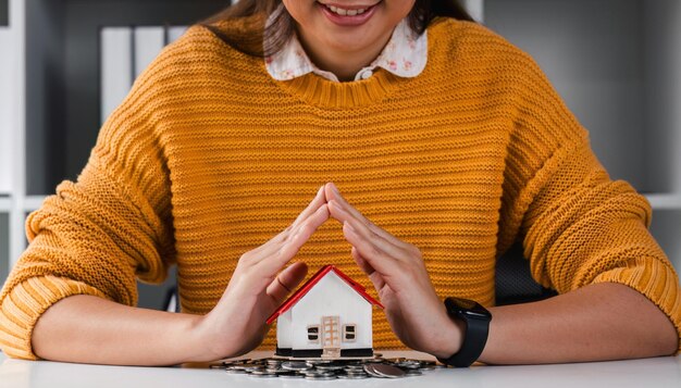 クローズアップの女性は、財産を象徴する手で小さな木造住宅の屋根を保護し、