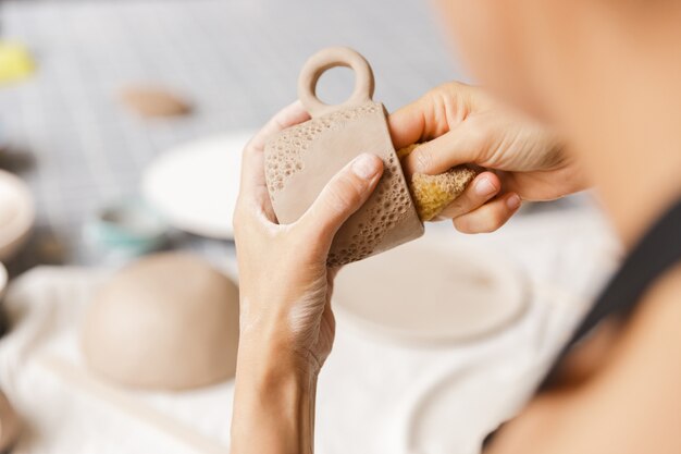 Close up of a woman making ceramic and pottery tableware at the workshop, working with clay