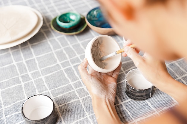 Foto primo piano di una donna che fa ceramiche e stoviglie in ceramica in officina, lavorando con l'argilla