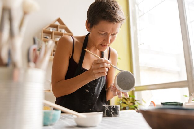 ワークショップで陶磁器や陶器の食器を作っている女性のクローズアップ、粘土で作業