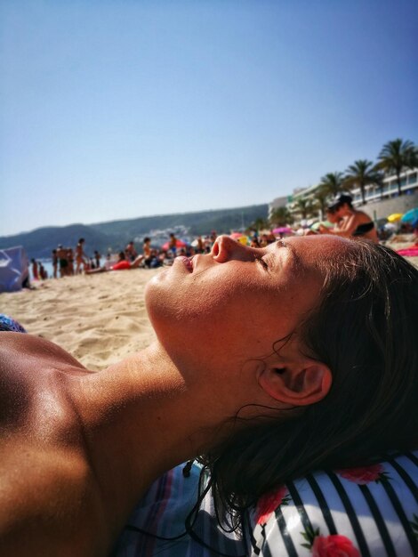 Foto close-up di una donna che fa un pisolino sulla spiaggia contro un cielo limpido durante una giornata di sole