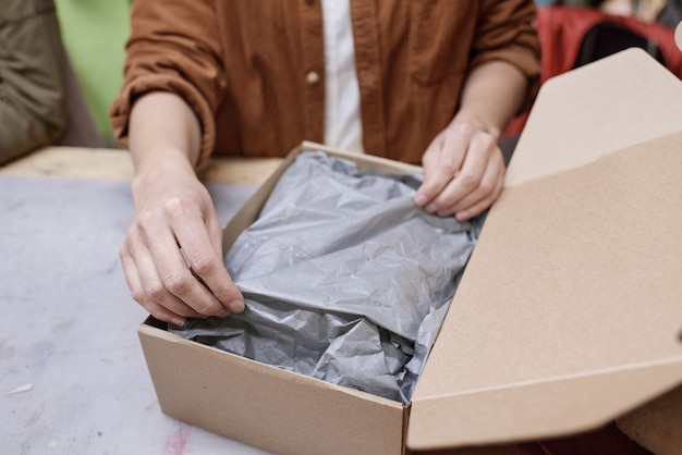 Close-up of woman packing things in box to deliver parcel to the customer