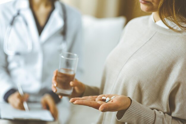 Close-up woman-patient holding pills near her doctor, time to take medications, cure for headache or remedy pain killer drugs. Stay at home concept during Coronavirus pandemic and self isolation quara