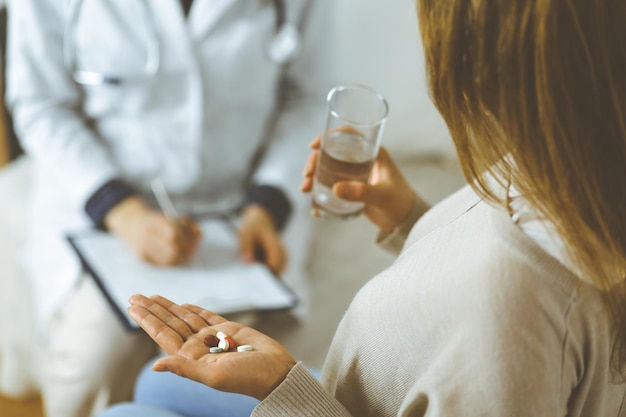 close-up woman-patient holding pills near her doctor, time to take medications, cure for headache or remedy pain killer drugs. stay at home concept during coronavirus pandemic and self isolation quara