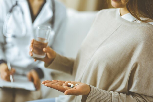 close-up woman-patient holding pills near her doctor, time to take medications, cure for headache or remedy pain killer drugs. stay at home concept during coronavirus pandemic and self isolation quara
