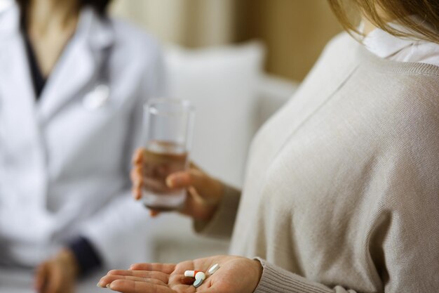 Close-up woman-patient holding pills near her doctor, time to take medications, cure for headache or remedy pain killer drugs. Stay at home concept during Coronavirus pandemic and self isolation quara