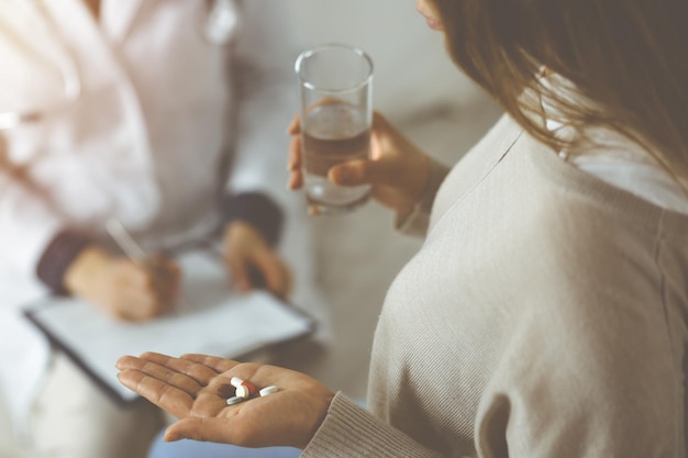 Close-up woman-patient holding pills near her doctor, time to take medications for headache. Stay at home concept during Coronavirus pandemic and self isolation quarantine. Covid 2019.