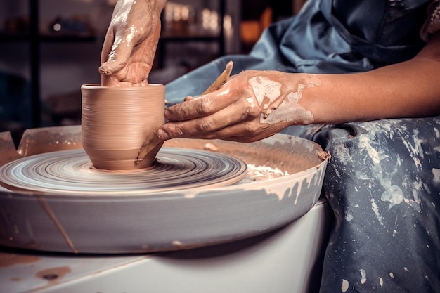 클로즈업 아름다운 작업장에서 한 여성 도예가가 깊은 갈색 점토 그릇을 조각하고 도공의 물레에 있는 과도한 점토를 잘라냅니다