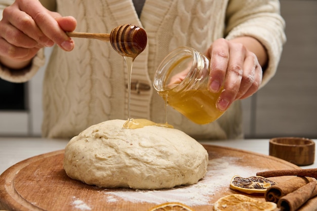 Close-up woman preparing gingerbread dough, holding a wooden stick and pouring some honey on pastry