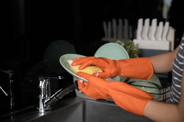 Фото Женщина в защитных перчатках стирает посуду губкой в кухонной раковине