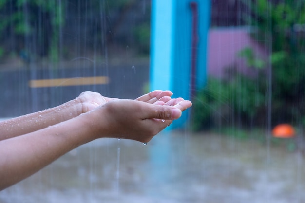 雨の中に彼女の手を入れている女性のクローズアップ雨、水の滴をつかまえる概念。