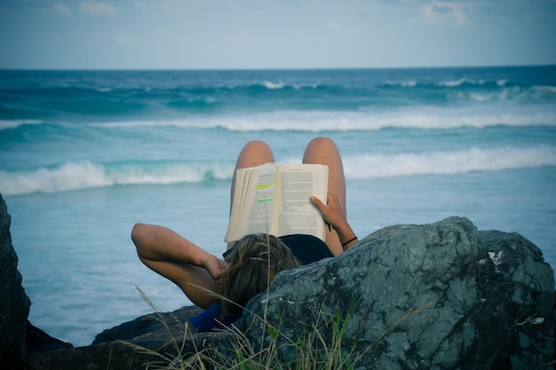 Foto close-up di una donna che legge un libro in mare contro il cielo