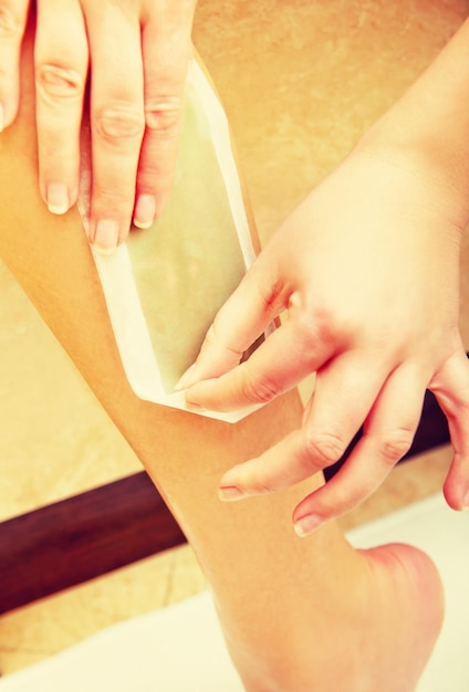 Close-up of woman removing hair on leg with wax strip