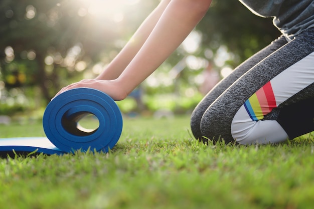 close up woman rolling yoga mat after working out at park