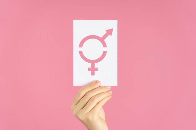 Close-up of a woman\'s hand holding a card with a symbol of\
gender equality on a pink background