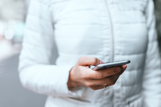 Chiuda in su della mano della donna che tiene smartphone grigio e sito di scorrimento sulla strada.