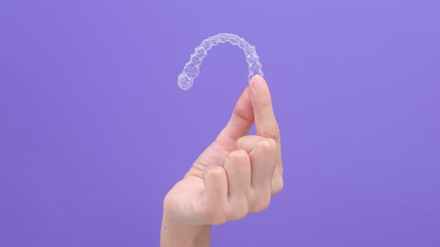 Close up of woman's hand holding invisalign braces in studio, dental healthcare and Orthodontic concept.