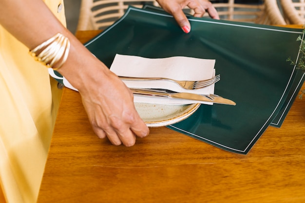 Close-up of woman's hand holding plate; cutlery and placemat from wooden table