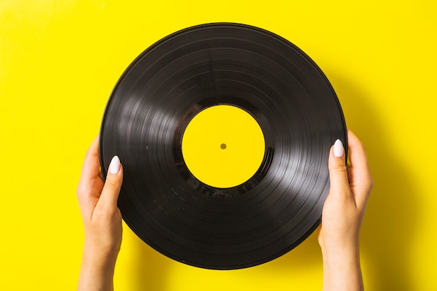 Primo piano dell'annotazione di vinile della tenuta della mano della donna su fondo giallo