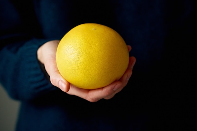 Close-up of woman's hand holding whole white yellow bright citrus fruit grapefruit on dark