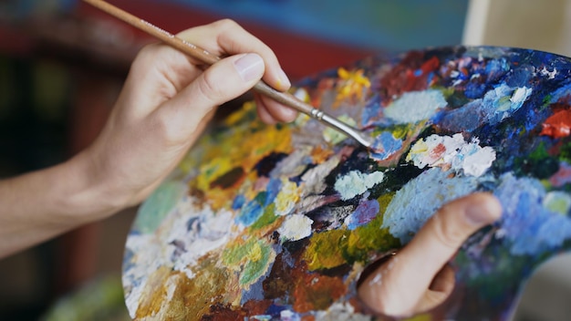 Close up of woman's hand mix paints with brush in palette in artclass