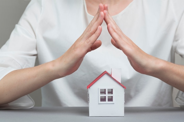 Close-up of woman's hand protecting house model on grey surface