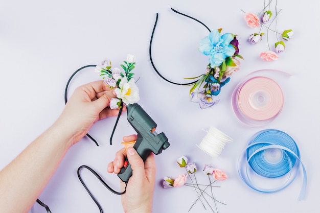 Foto primo piano della mano della donna che attacca i fiori sul fermaglio per capelli con la pistola di colla calda elettrica sul contesto bianco