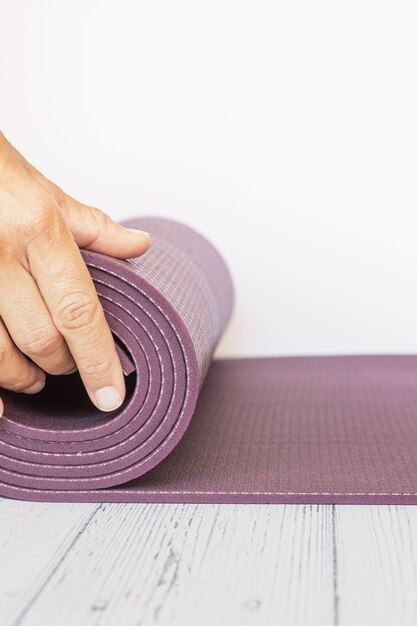 Close-up of a woman's hand unfolding a violet yoga mat on white wood