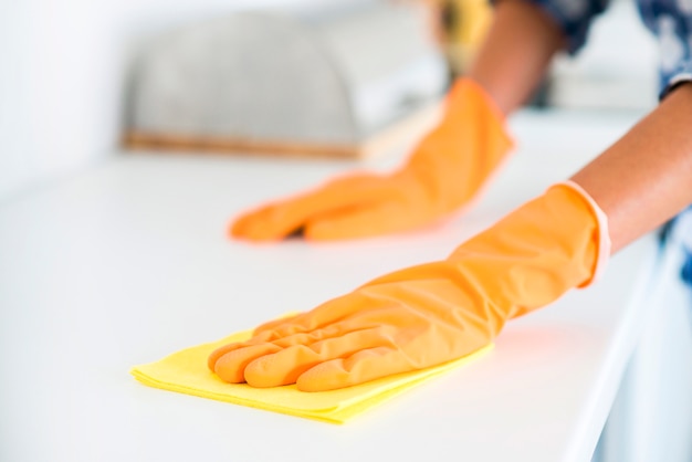 Close-up of woman 's hand wipes white table with yellow napkin