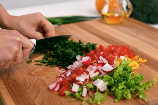 Foto primo piano delle mani della donna che cucinano in cucina. casalinga che affetta l'insalata fresca concetto di cucina vegetariana e sana.