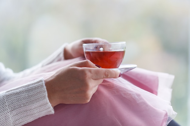 Close up of woman's hands holding a cup of tea, wearing a white sweater and enjoying the leisure time