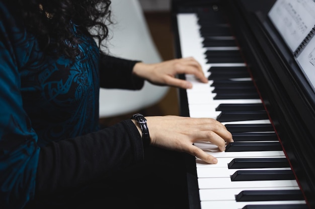 Close up of woman's hands playing piano by reading sheet music. Selective focus