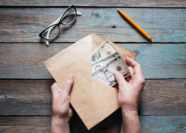 Photo close up of woman's hands puts american dollar bills in an envelope on wooden desktop