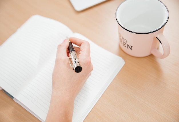 Close up of a woman's hands writing in a notepad placed on a wooden table home office and work concept plans and thoughts