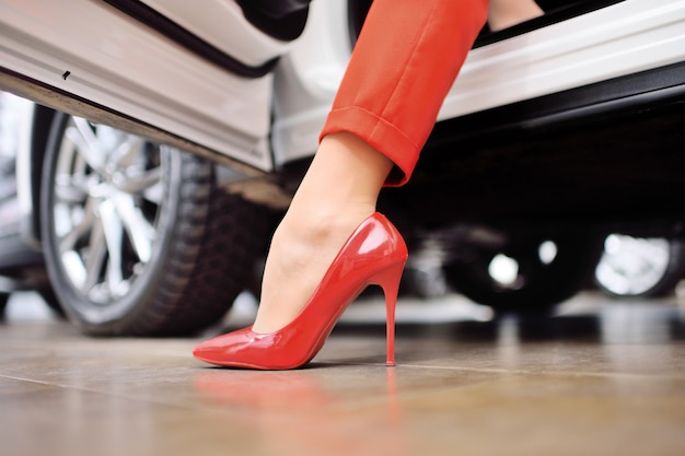 Close-up of a woman's leg in a red suit and red shoes against the surface of a car